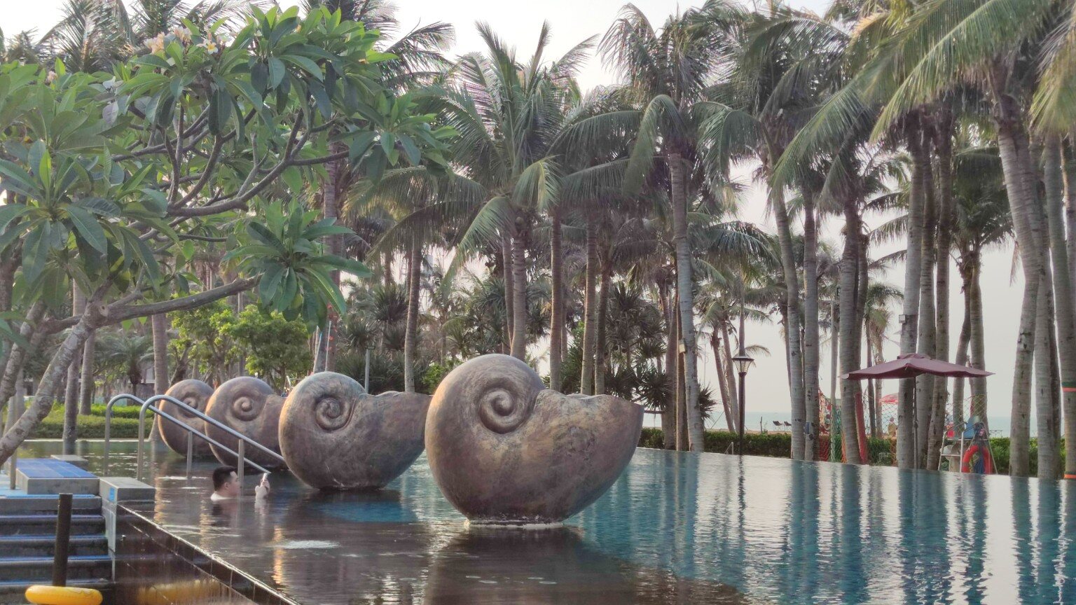 Swimming pool with large snail sculptures and palm trees in Haikou